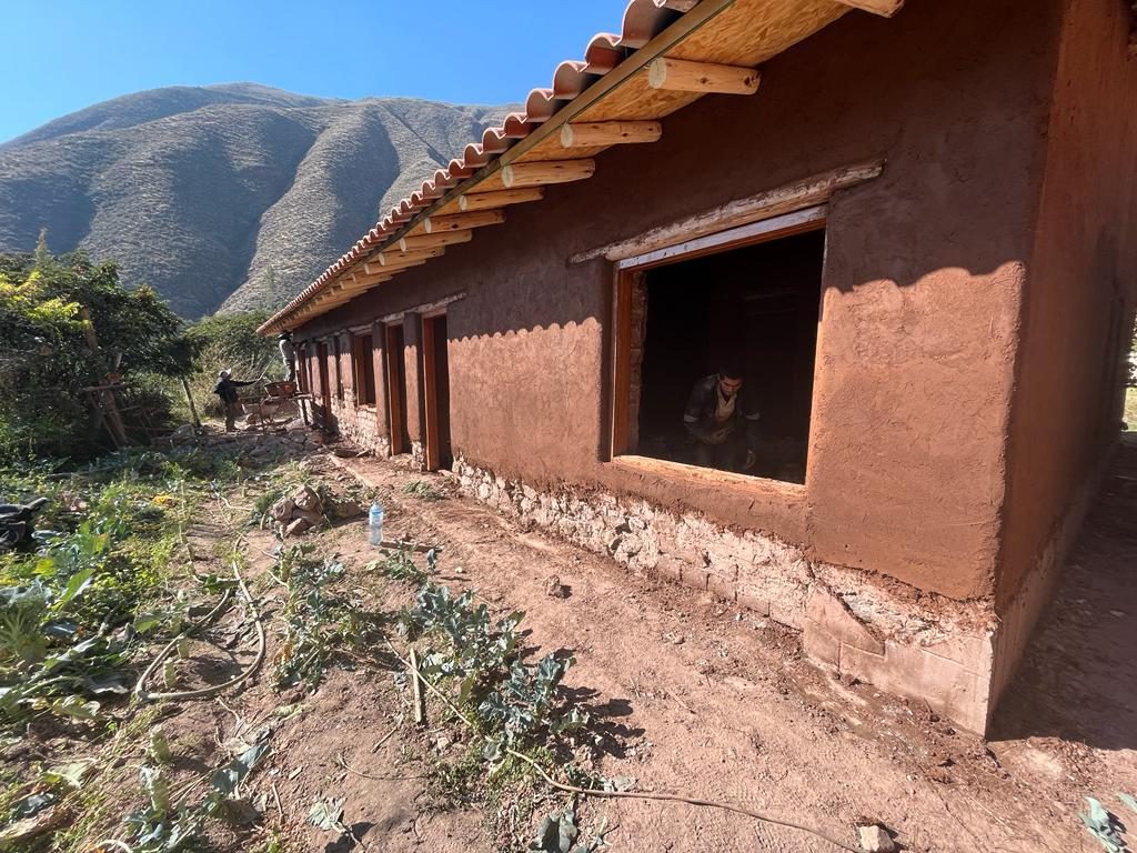 Muros de barro recién revocados bajo un techo de tejas, con montañas detrás